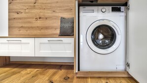 Une petite buanderie équipée d’un lave-linge à chargement frontal, d’un plancher en bois et d’un meuble blanc avec des tiroirs.