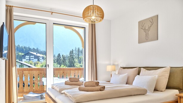 Une chambre avec un lit en bois, une vue sur l’extérieur et un luminaire au plafond.