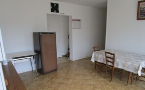 A compact kitchen with a refrigerator, a dining table with chairs, and a calendar on the wall.