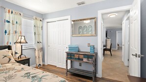 A bedroom with a bed, a nightstand, a dresser, a mirror, and a door leading to another room. - Come Stay In This Charming & Cozy Home In The Heart Of Naples (Naples)