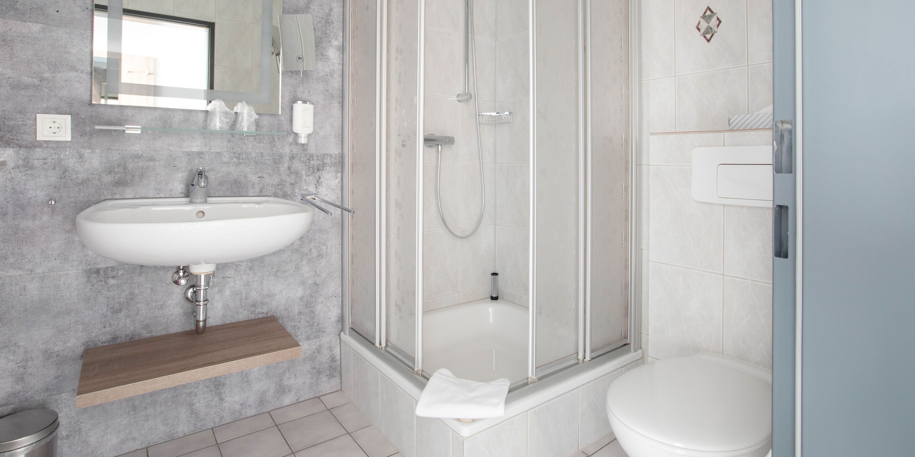 A modern bathroom with a white sink, a glass-enclosed shower, and a toilet.