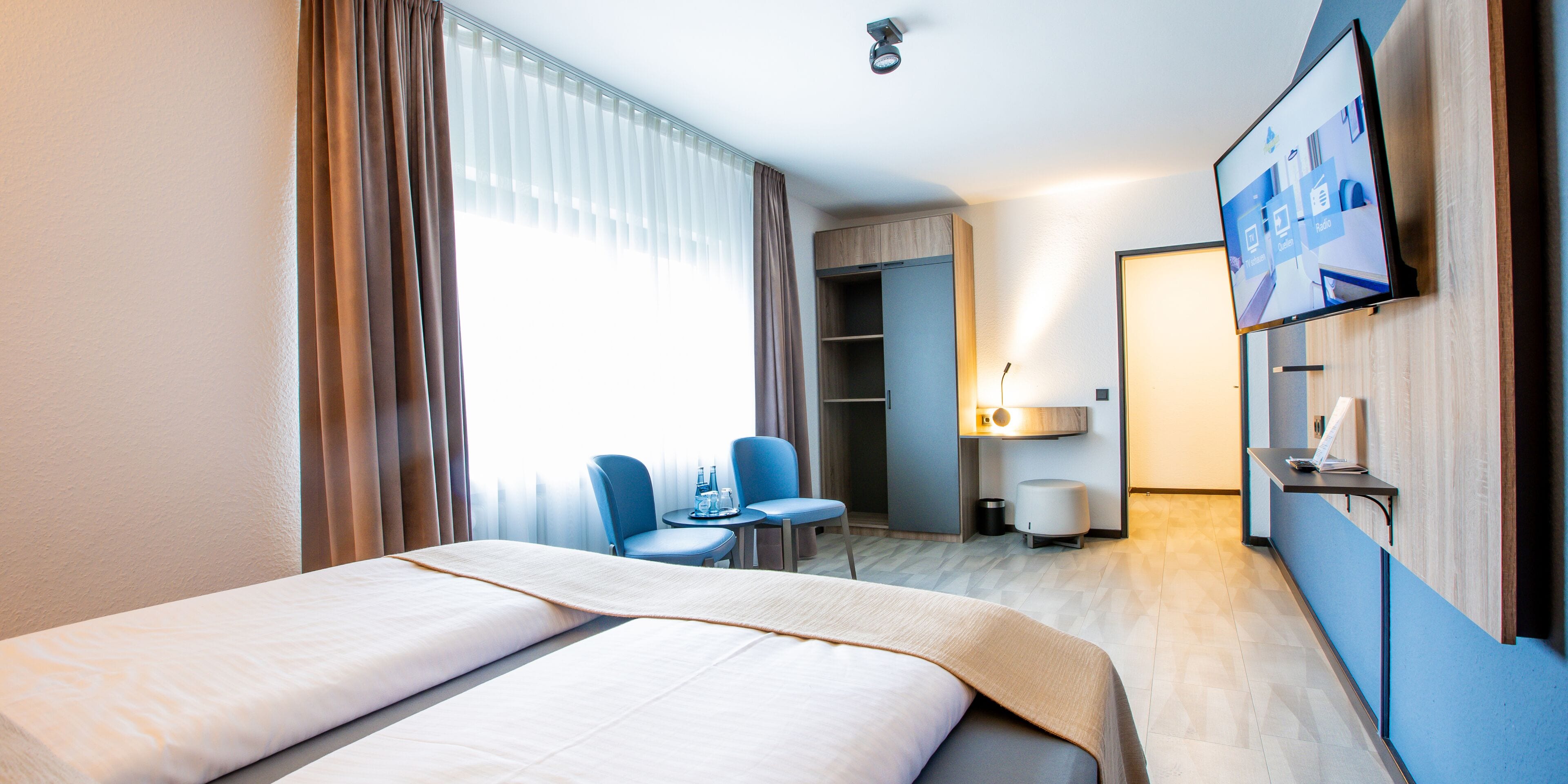 A hotel room with a bed, a desk, a chair, a TV, and a wardrobe.