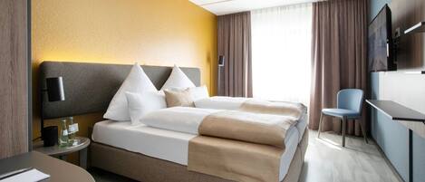 Habitación de hotel con cama, mesita de noche, silla y televisión montada en la pared.