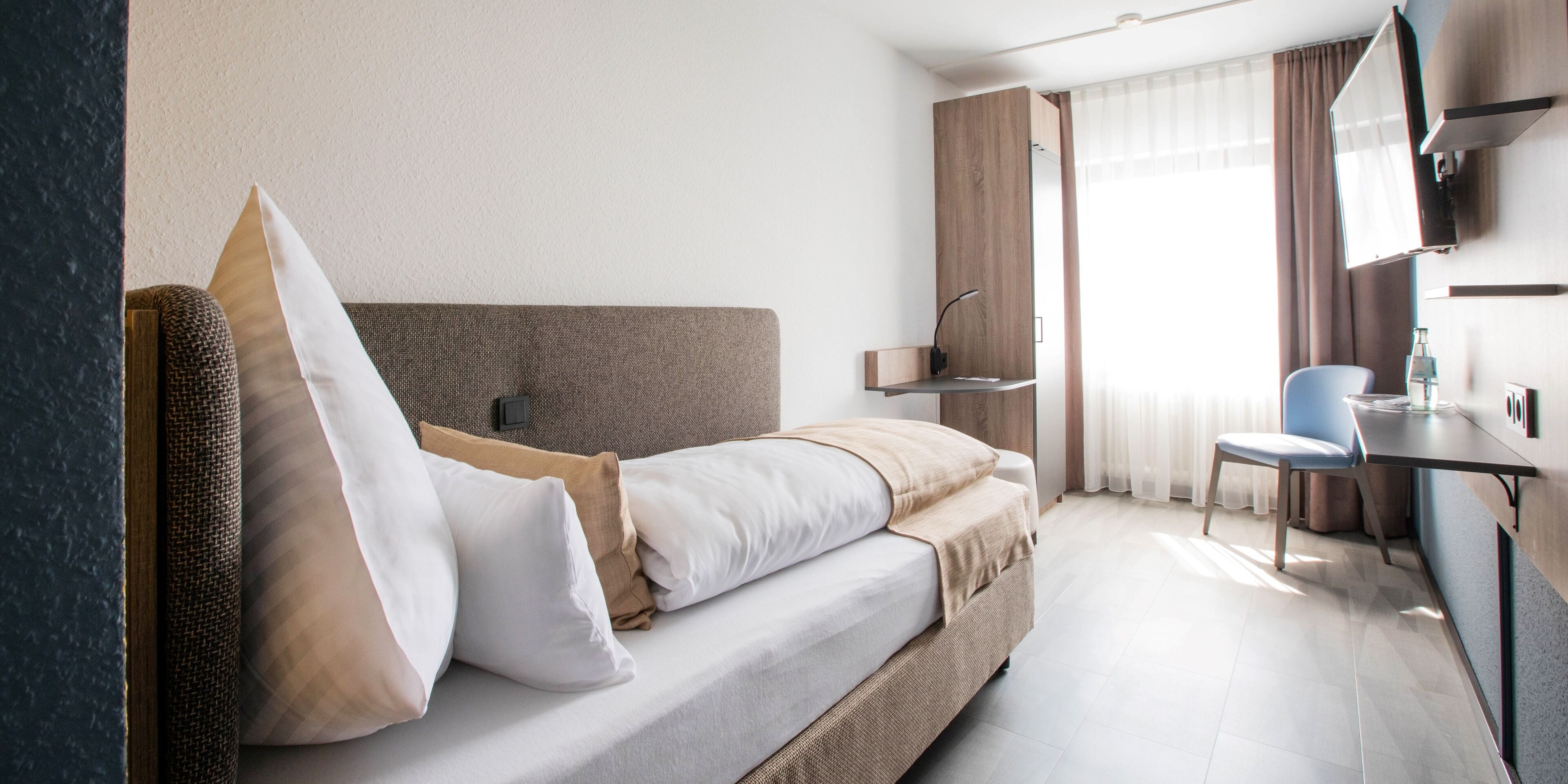 Une chambre d’hôtel moderne équipée d’un lit, d’un bureau, d’une chaise et d’un téléviseur.
