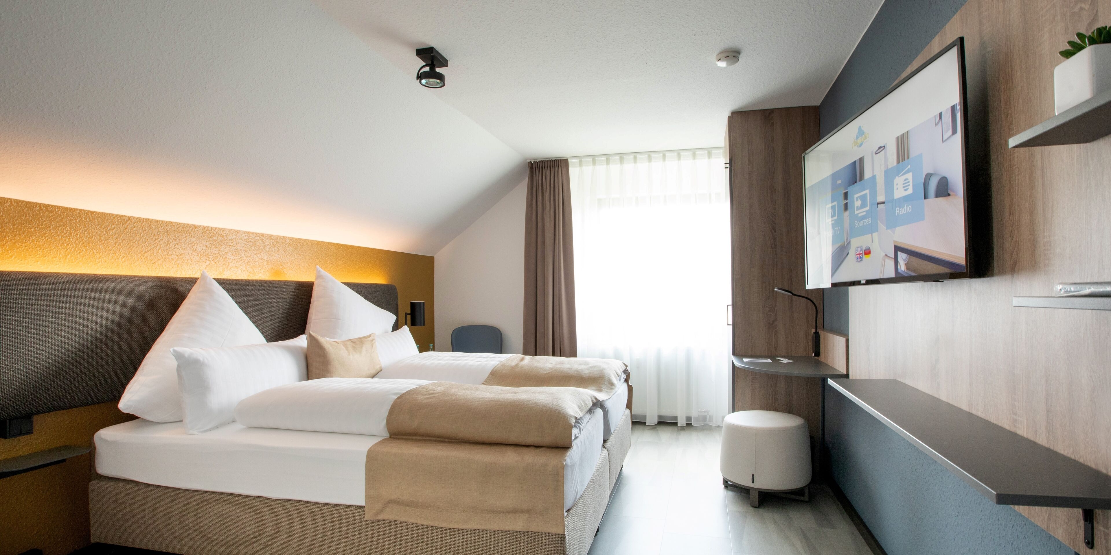 Une chambre d’hôtel comprenant un lit, une table de chevet, une télévision et un bureau avec une chaise.