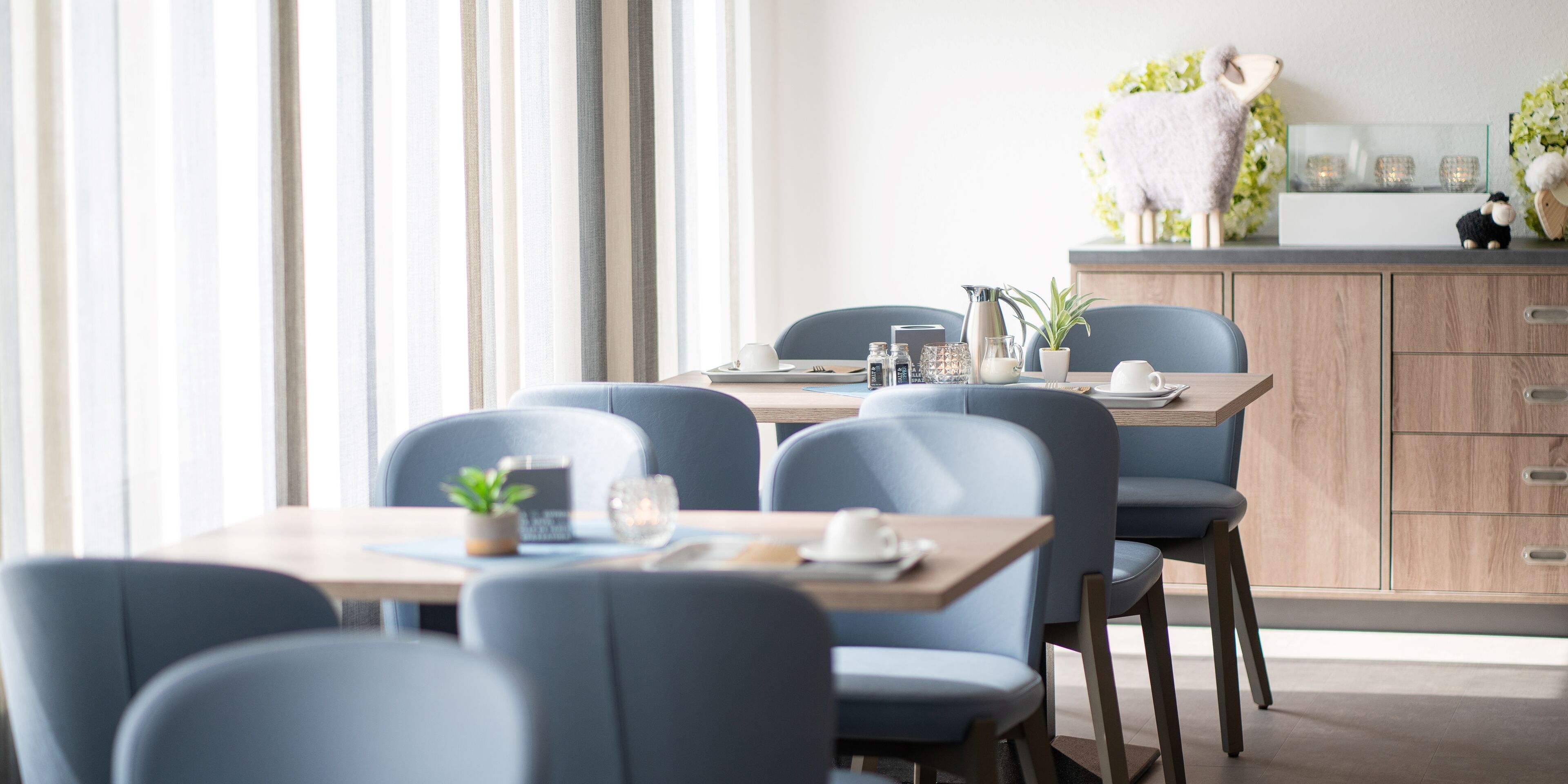 Un comedor moderno con una mesa de madera, sillas azules y una oveja decorativa en la encimera.