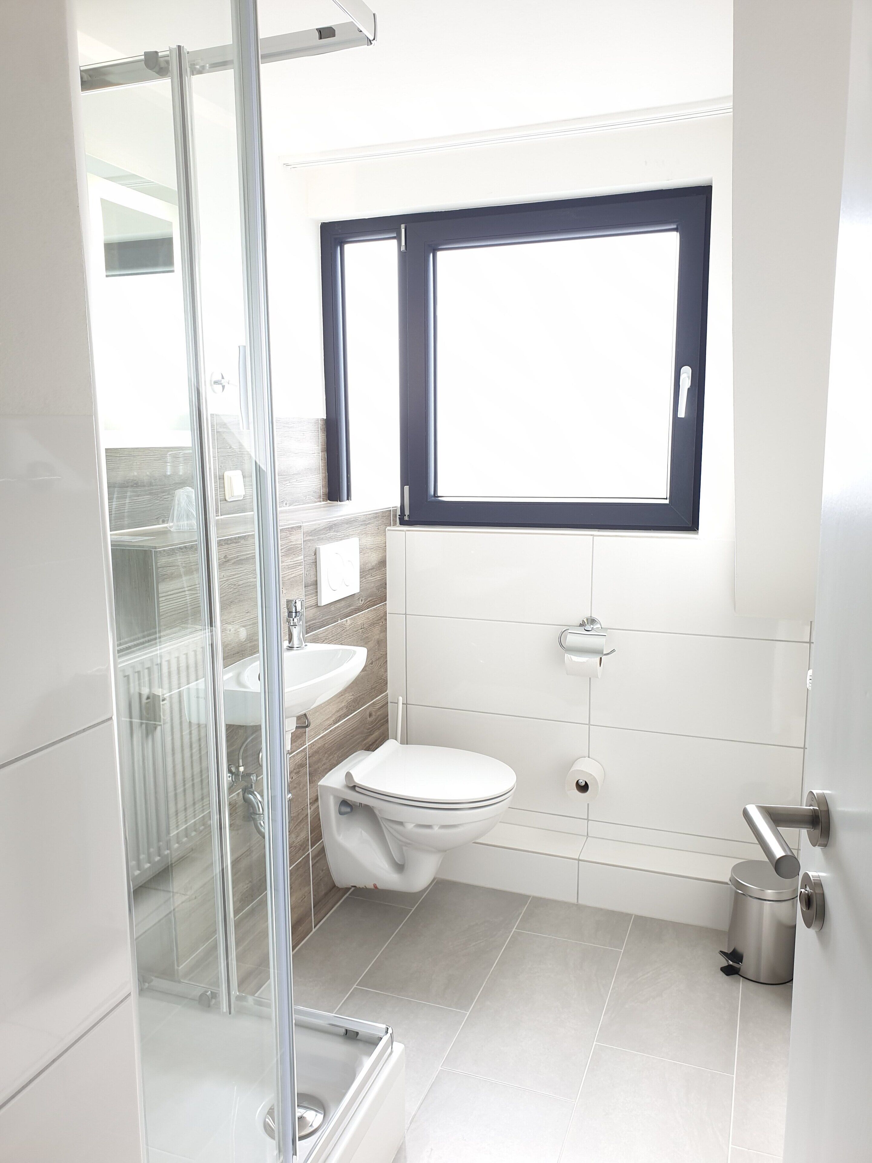 A modern bathroom with a glass shower enclosure, a white sink, a toilet, and a window above the toilet.