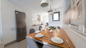 Une cuisine moderne avec une table à manger pour deux personnes, un réfrigérateur et une fenêtre donnant sur un paysage agréable.