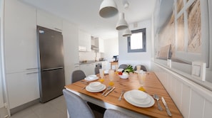 A modern kitchen with a dining table set for two, a refrigerator, and a window with a view.
