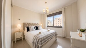 Une chambre d’hôtel avec un lit, une table de chevet, une lampe, une fenêtre et un petit bureau agrémenté d’une plante.