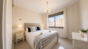 Habitació d'hotel amb llit, taulella de nit, làmpada, finestra i una petita taula amb una planta.