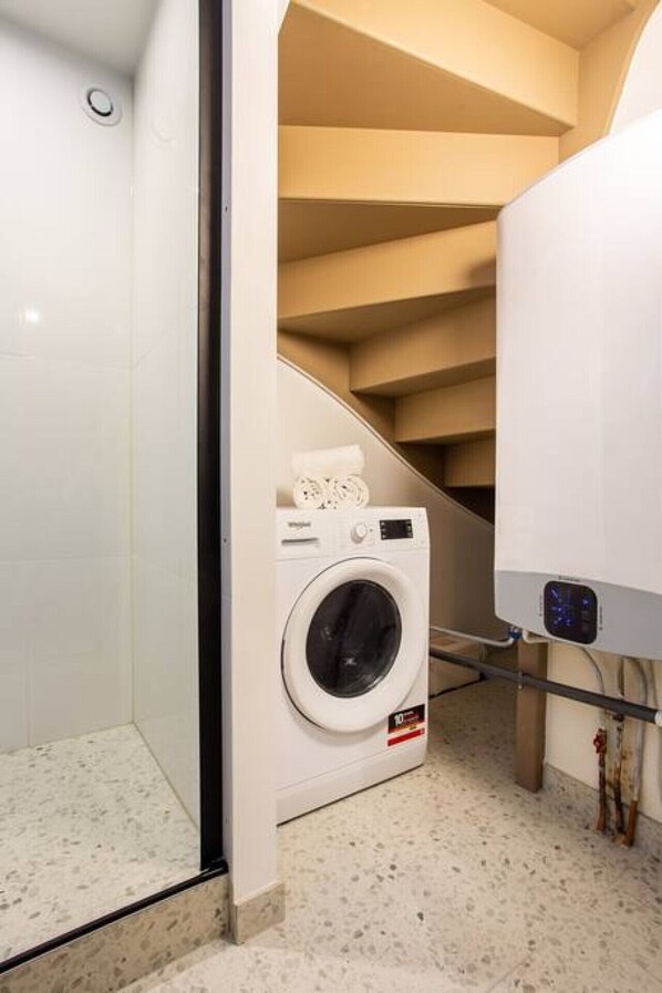 Une petite buanderie comprenant un lave-linge, un sèche-linge et un petit espace douche.