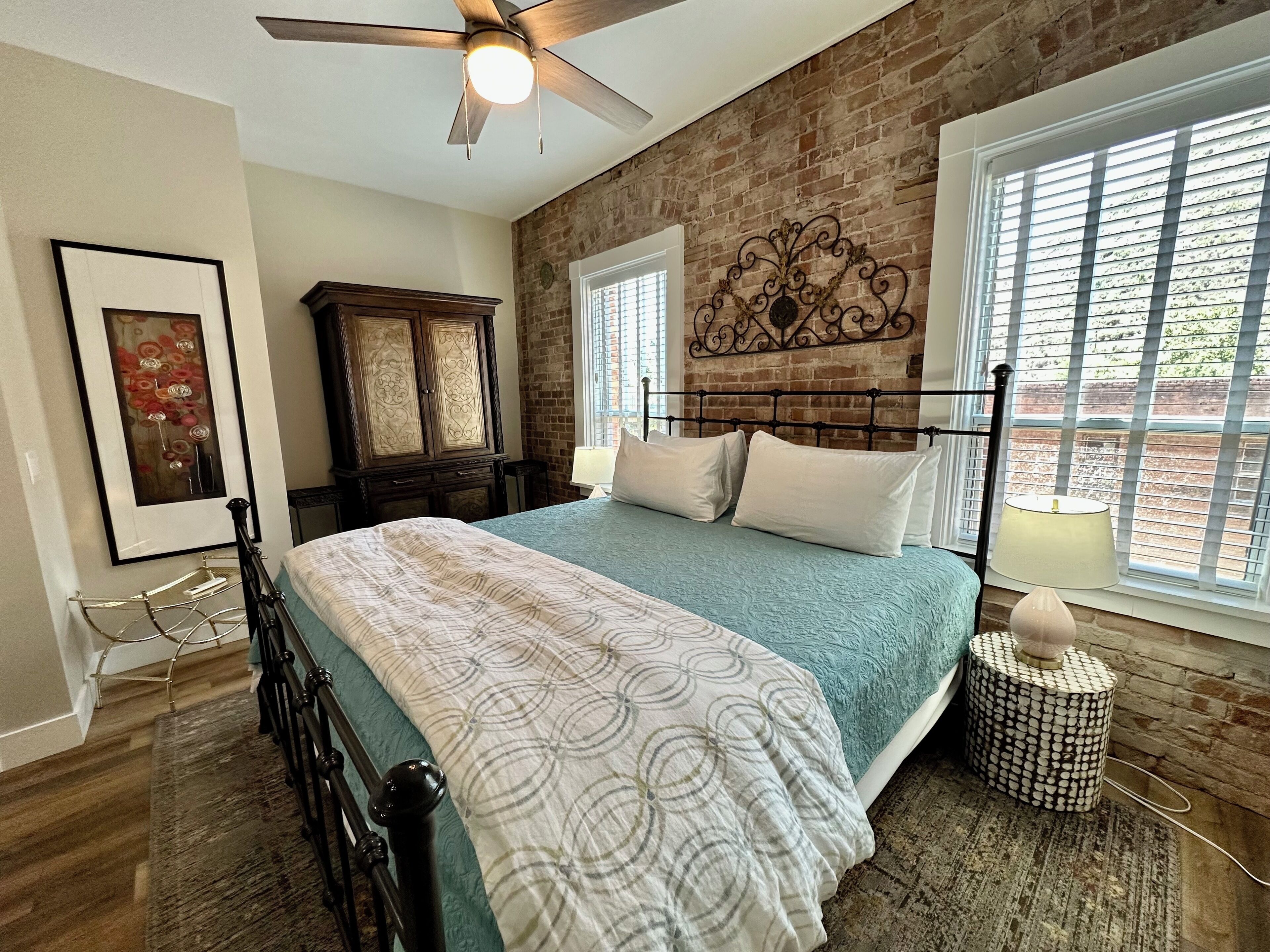 A bedroom with a bed, a ceiling fan, a dresser, a window with blinds, and a decorative wall piece.