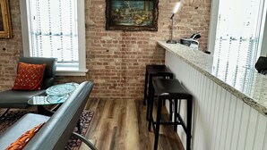 Een compacte keuken met een bakstenen muur, een zithoek met een bank en stoelen, en een raam met jaloezieën.