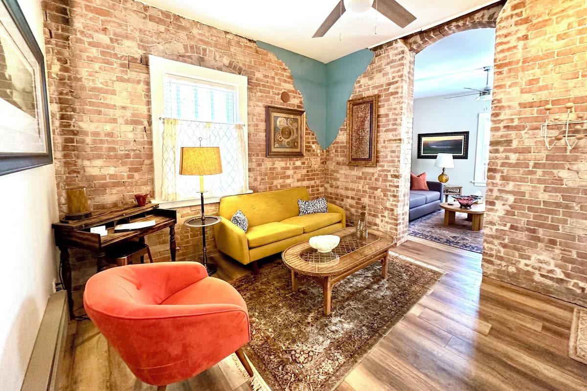 A living room with a yellow sofa, a red chair, a coffee table, and a ceiling fan.