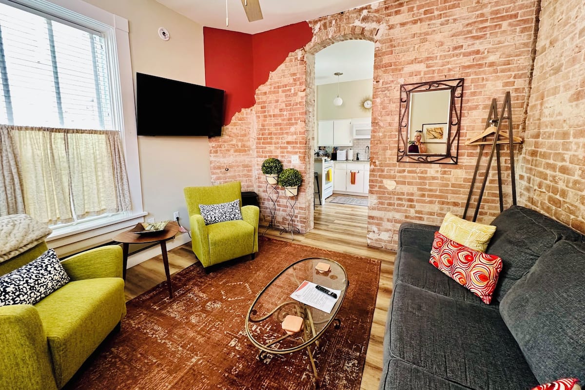 A living room with a brick wall, a green armchair, a grey sofa, and a coffee table.