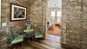 Een eetruimte met een bakstenen muur, een lijst met bloemerkunst, een tafel met stoelen en een uitzicht op een andere kamer met een plafondventilator.