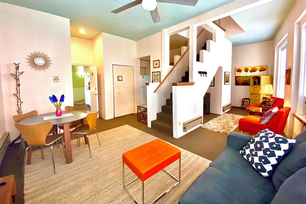 A spacious living area with a dining table, chairs, a sofa, and a staircase leading to an upper floor.