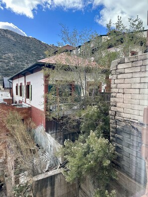 A residential area with a house featuring a red brick wall, a white facade, and a pink roof. There is a concrete wall in the foreground, and a mountain is visible in the background. - Bisbee Brownstone Suites (Bisbee)