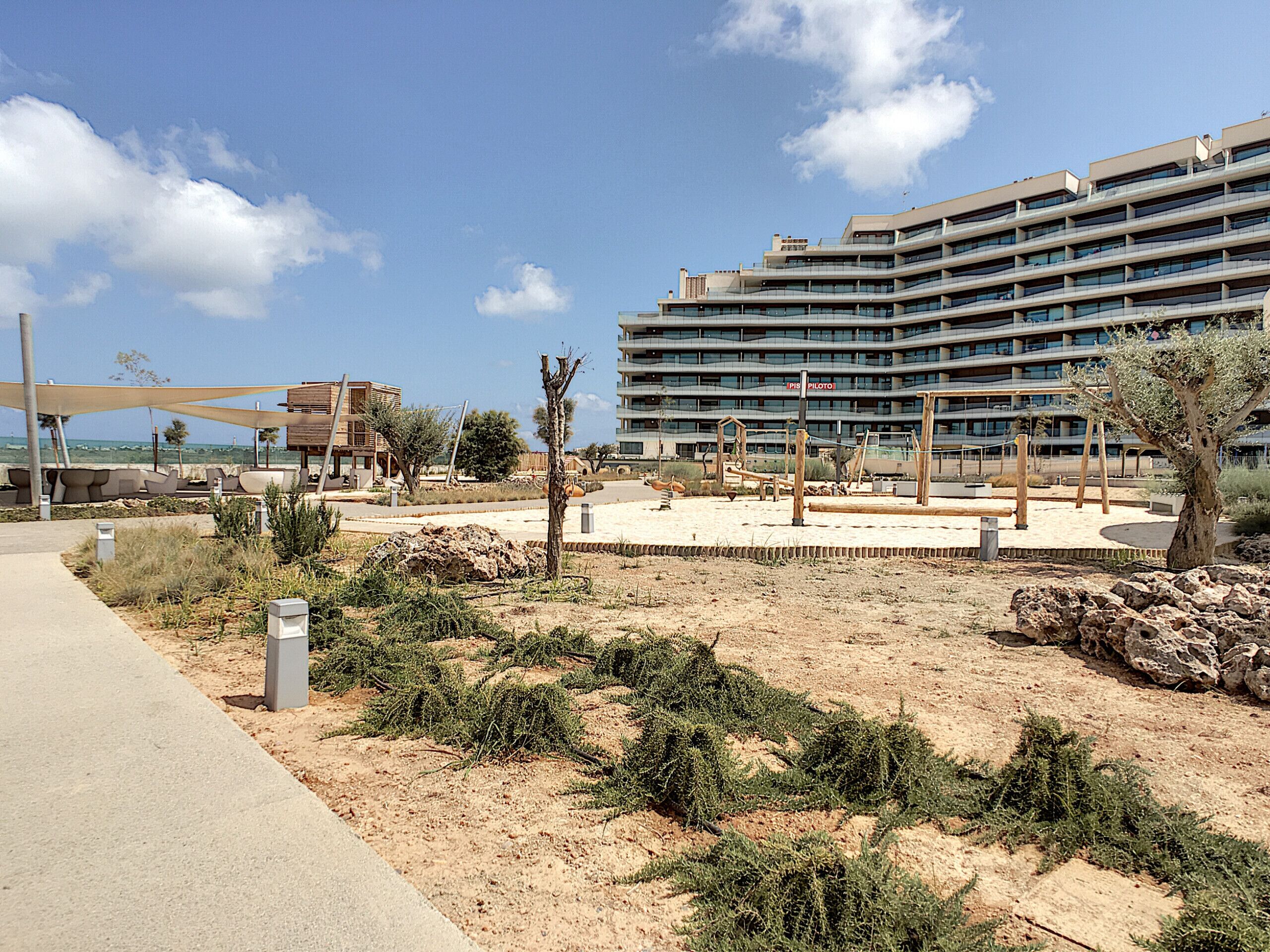 Un hôtel moderne à l’architecture imposante, doté d’un espace extérieur aménagé et surplombant un paysage sablonneux à la végétation clairsemée.