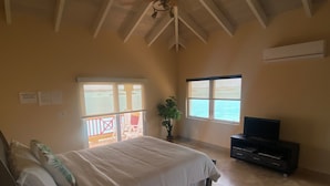 A bedroom with a bed, a TV, a potted plant, and a view of the sea. - The Four Breezes With Pool and View (providenciales)