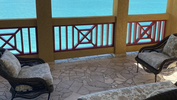 A covered outdoor seating area with wicker furniture and a view of turquoise waters and islands. - The Four Breezes With Pool and View (providenciales)