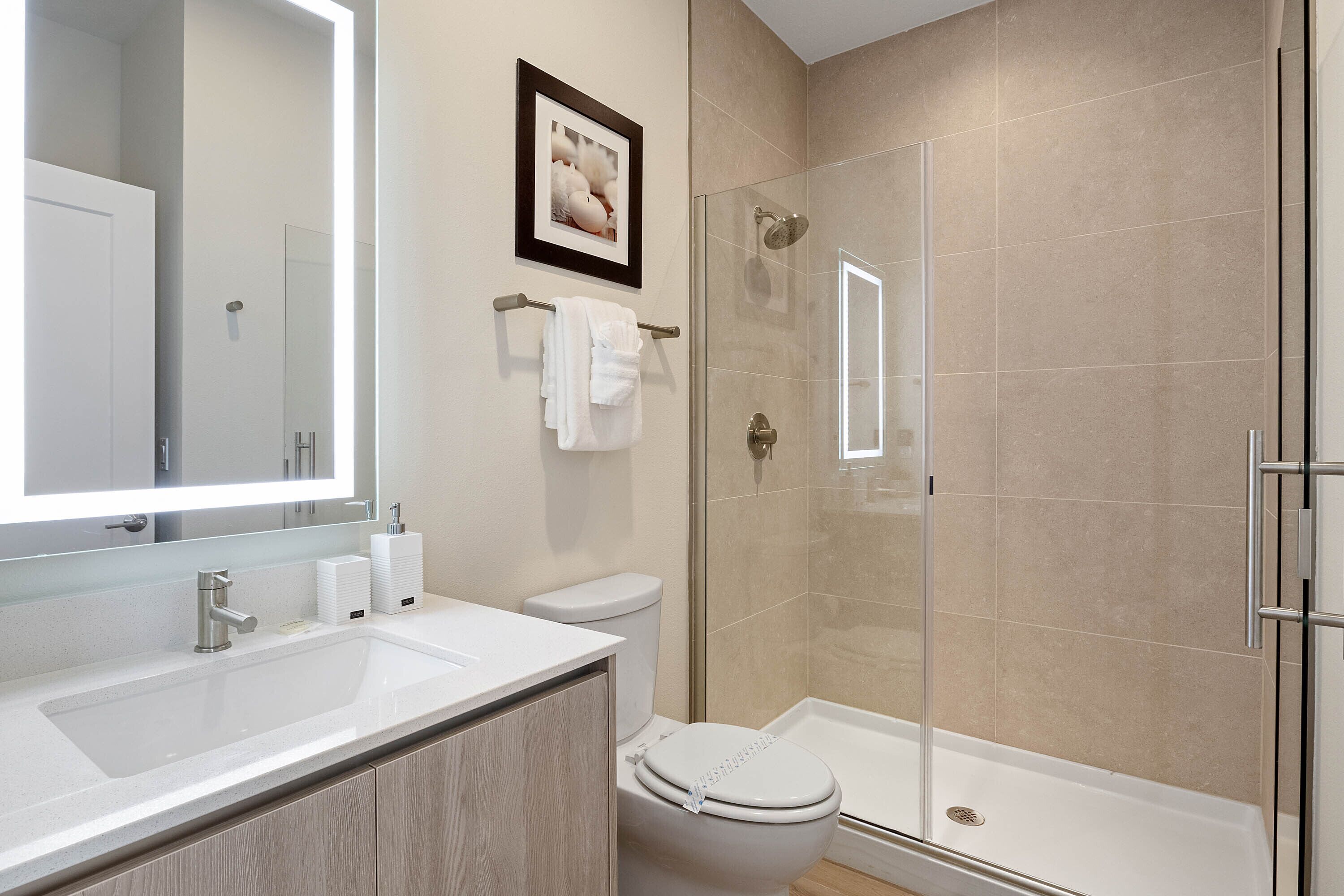 A modern bathroom with a large mirror, white sink, toilet, and glass-enclosed shower.