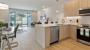 Cozinha moderna com ilha central, eletrodomésticos de aço inoxidável e área de refeições com mesa e cadeiras de vidro.