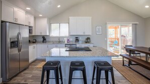 Une cuisine moderne dotée d’un grand îlot central, d’appareils électroménagers en acier inoxydable et d’un coin repas avec un banc.