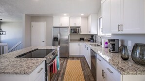 Une cuisine moderne avec des meubles blancs, des appareils en acier inoxydable, des comptoirs en granit et un tapis jaune à motifs.