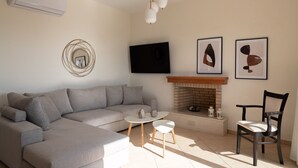 Ein modernes Wohnzimmer mit einem grauen Sofa, einem kleinen runden Tisch, einem Holzstuhl, einem Kamin und abstrakter Wandkunst.