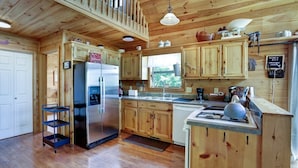 A wooden cabin kitchen with a refrigerator, stove, sink, and wooden cabinets.