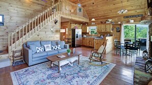 A spacious cabin with a wooden interior, a staircase leading to an upper level, a kitchen, and a dining area.
