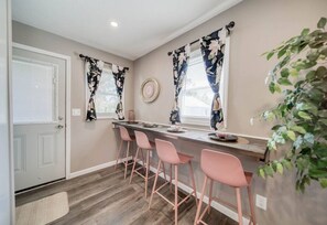 Une cuisine avec un coin bar, un plancher en bois, des tabourets de bar roses et des rideaux à motifs floraux.