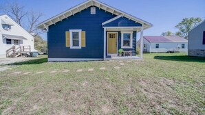 Une petite maison de plain-pied, à l’extérieur bleu foncé et aux volets jaunes, dotée d’un porche et d’un numéro de maison bien visible.
