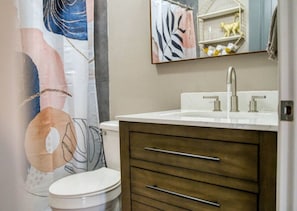 Une salle de bain avec des toilettes blanches, un meuble-lavabo en bois et un miroir au-dessus du meuble-lavabo.