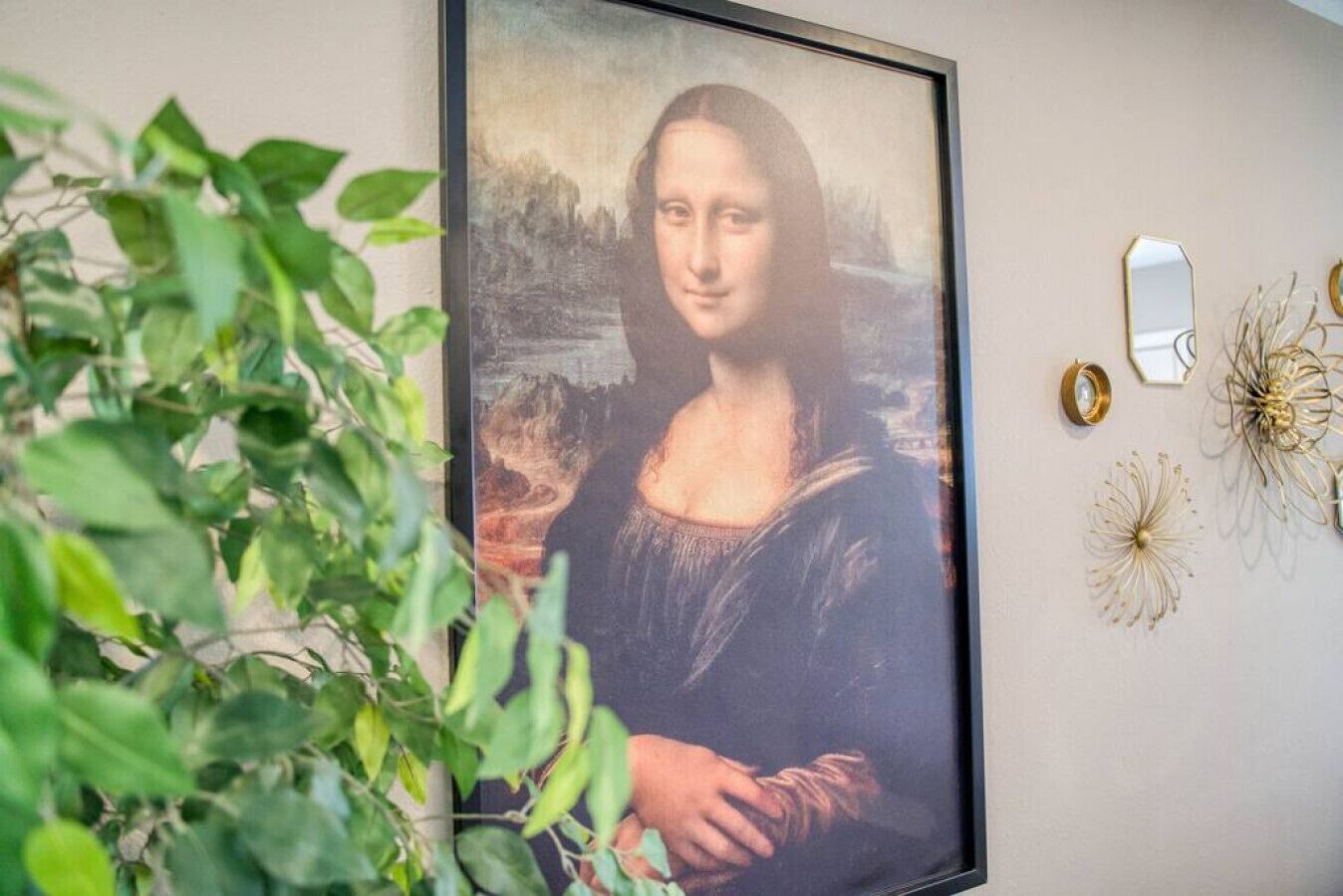 Une œuvre d’art encadrée est accrochée au mur, avec une plante placée au premier plan.