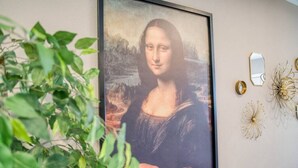 Une œuvre d’art encadrée est accrochée au mur, avec une plante placée au premier plan.