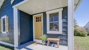 Une maison avec un porche à l’avant, une porte jaune, une fenêtre avec des volets et un petit banc en bois.