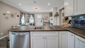 Una cucina moderna con mobili bianchi, una lavastoviglie in acciaio inossidabile e un piano di lavoro in legno scuro.