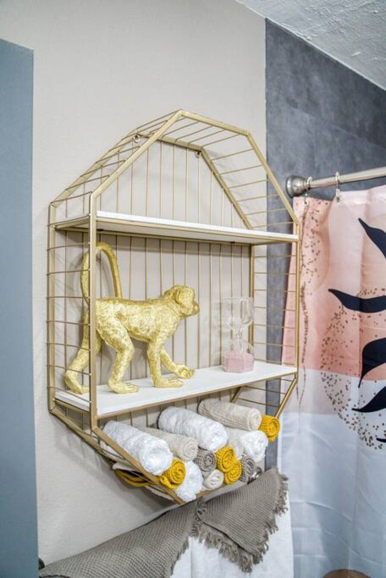 A room with a decorative metal shelf unit against the wall, holding a golden lion figurine, a glass, and folded towels.