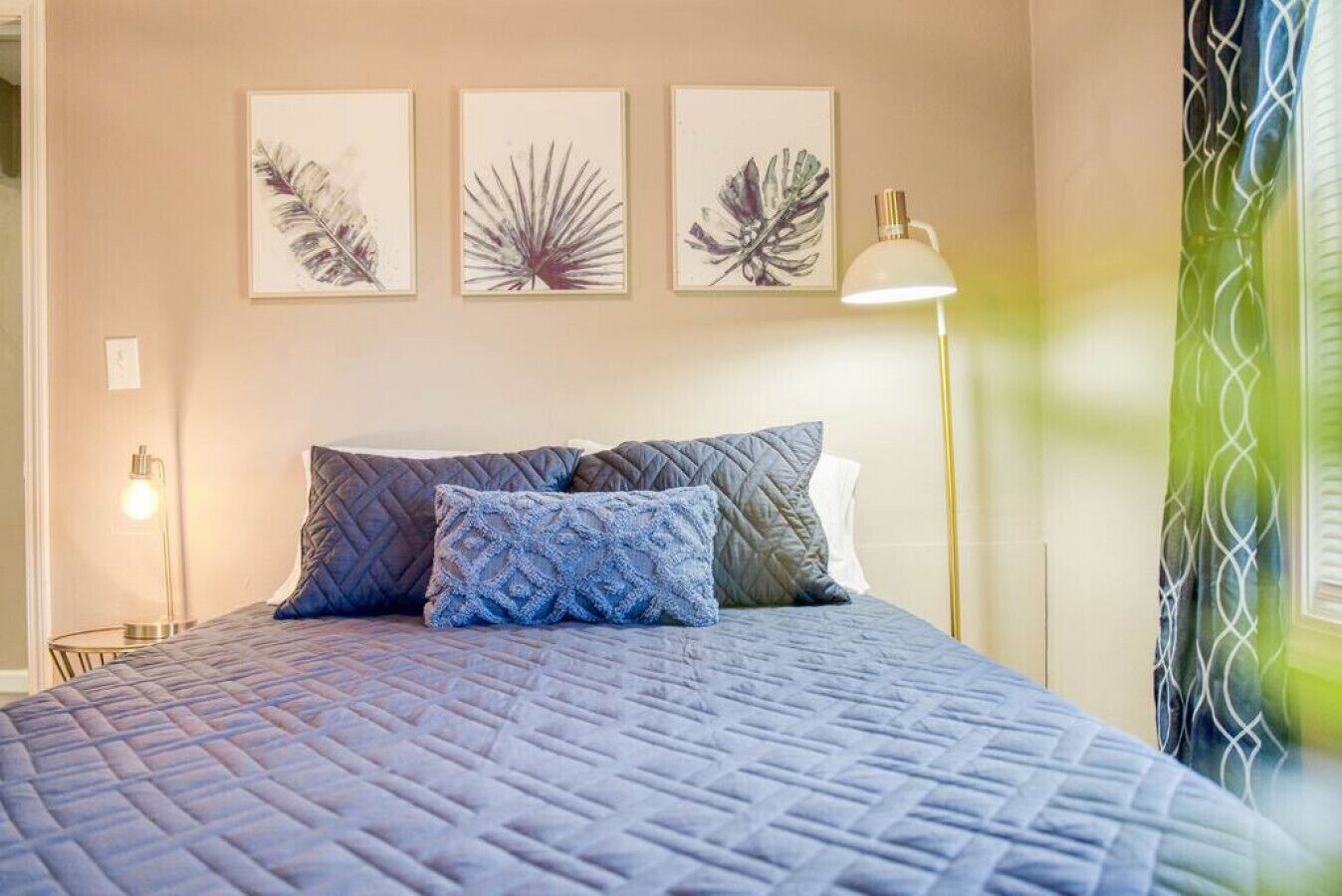 A bedroom with a bed, pillows, a bedside lamp, and wall art.