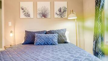 A bedroom with a bed, pillows, a bedside lamp, and wall art.