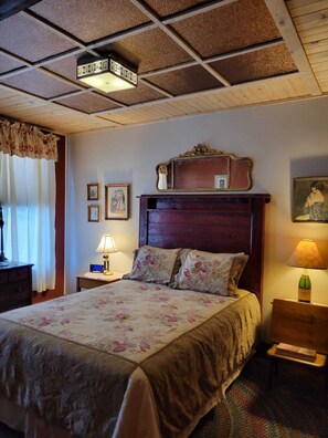 Una camera da letto con una testiera in legno, copriletto floreale, un comodino con una lampada e uno specchio sopra il letto.