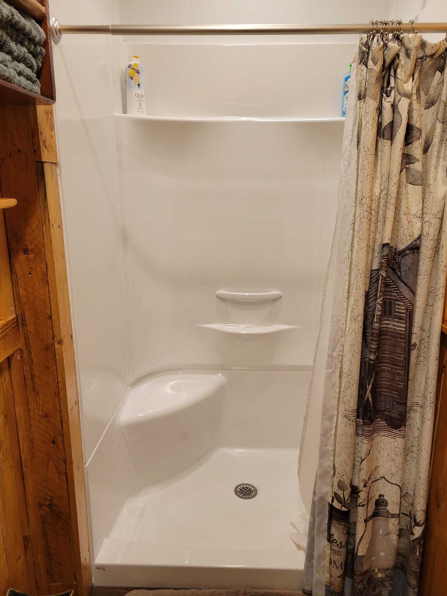 Une douche avec un drain, une étagère et un rideau de douche à motifs marins.