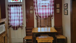 Un espace repas avec une table et des chaises en bois, un panneau de sortie rouge et une fenêtre ornée d’un rideau à carreaux.