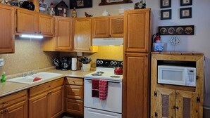 Une cuisine dotée de meubles de rangement en bois, d’une cuisinière, d’un four à micro-ondes et de divers ustensiles de cuisine.