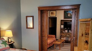 Une pièce confortable avec un grand lit, une porte en bois donnant sur un couloir, une petite table et une bibliothèque.
