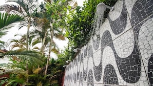 Pared de azulejos con un mosaico agrietado, rodeada de exuberante vegetación tropical.