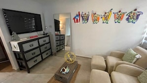 Un salon avec un canapé beige, un meuble de rangement noir pour appareils électroniques, un téléviseur et des œuvres d’art décoratives accrochées au mur.